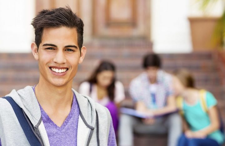 Portrait of confident student smiling with classmates sitting in background on college campus. Horizontal shot.
